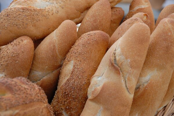 Una selección de panes baguette frescos, algunos espolvoreados con semillas de sésamo, apilados en una canasta.