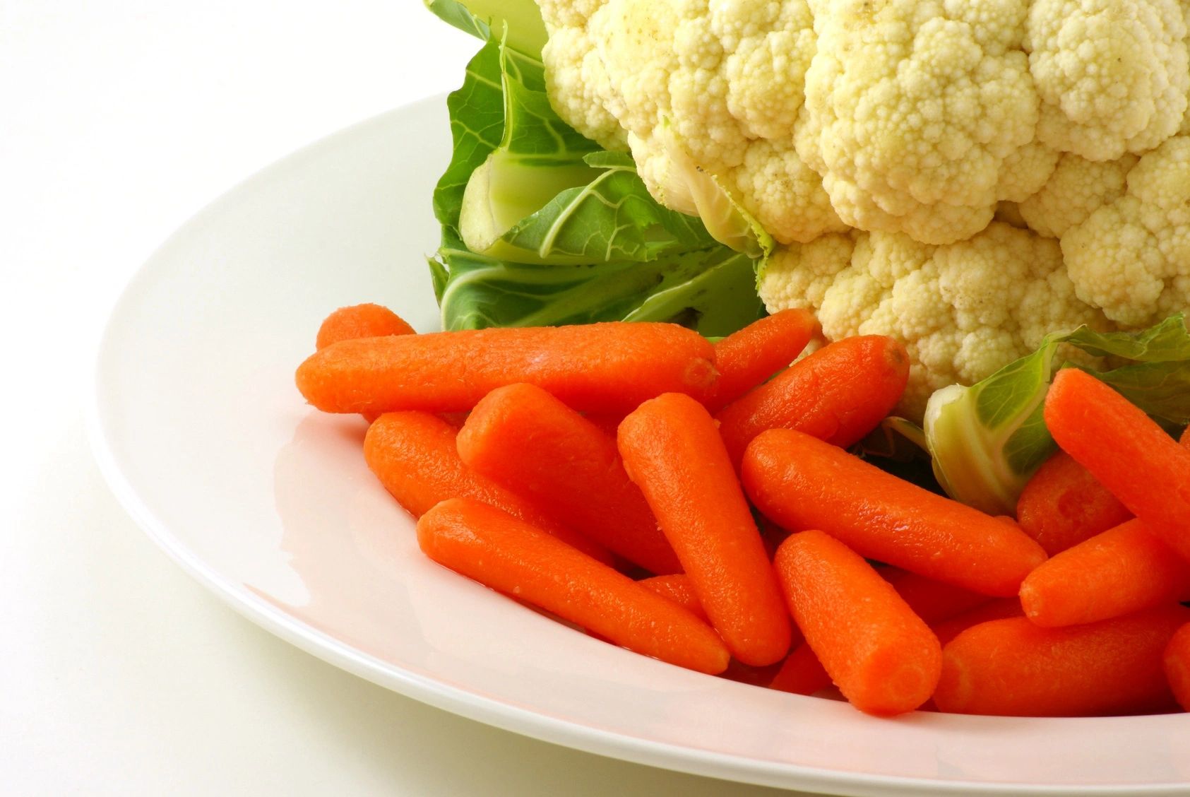 Plato con zanahorias baby y una cabeza de coliflor, presentados sobre un fondo blanco para un aspecto fresco y saludable.