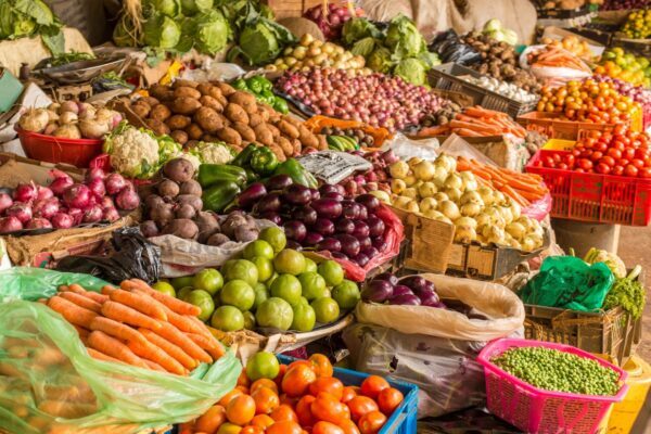 Puesto de mercado vibrante y colorido lleno de una variedad de verduras frescas como zanahorias, tomates, limas y patatas.