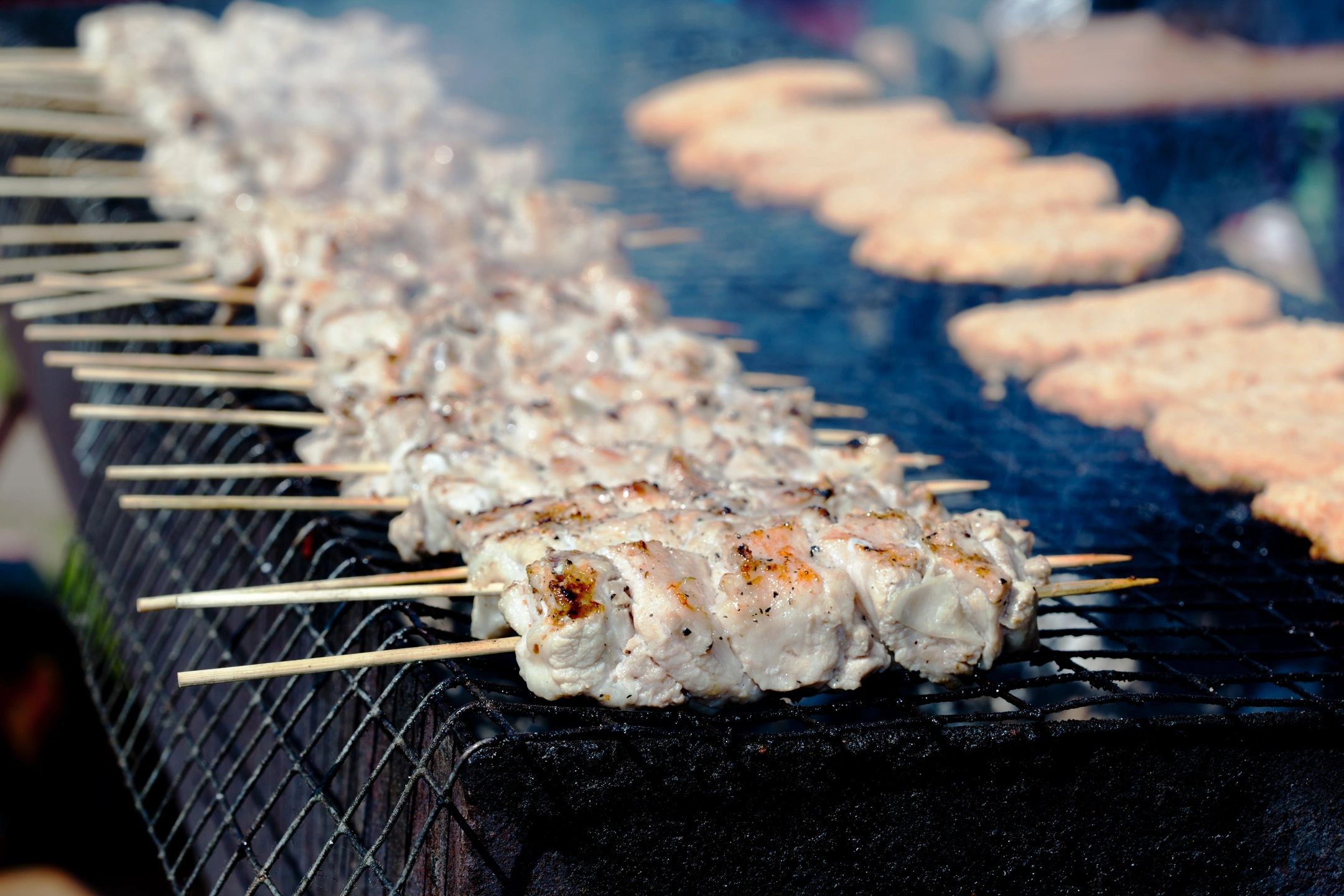 Pinchos de carne cocinándose en una parrilla al aire libre.