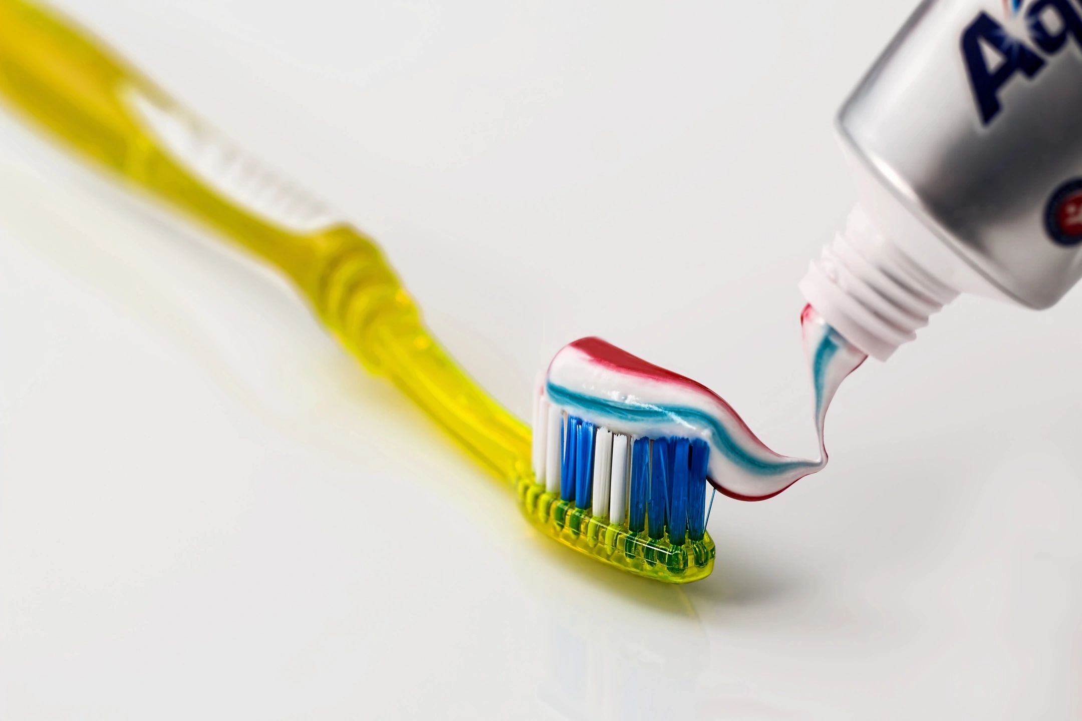 Pasta de dientes multicolor siendo aplicada a un cepillo de dientes amarillo.