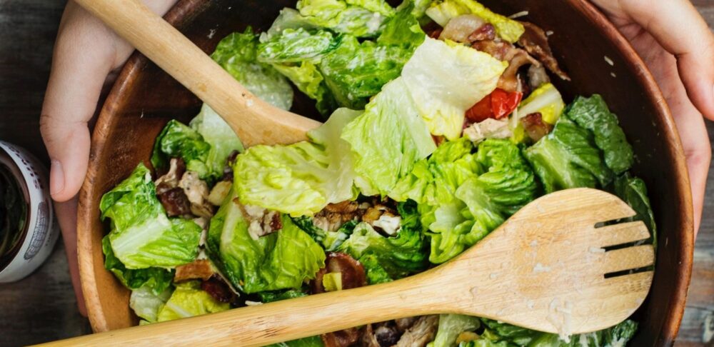 Manos mezclando una ensalada fresca en un tazón de madera.