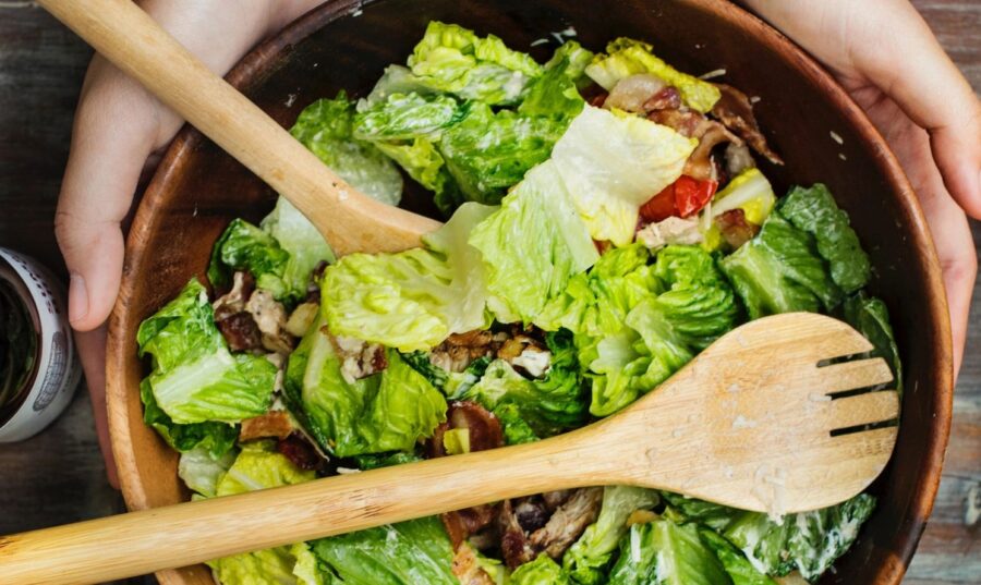 Manos mezclando una ensalada fresca en un tazón de madera.