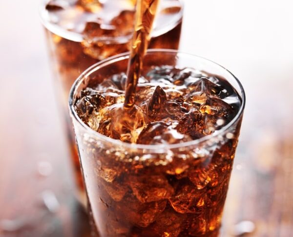 Refresco de cola siendo vertido en un vaso con hielo.