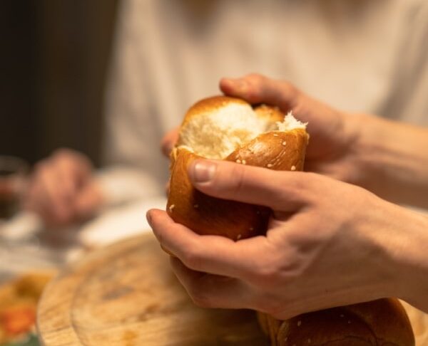 Manos partiendo un pan fresco en una mesa de cena.