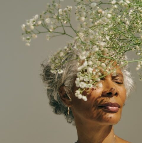 Una mujer mayor con el pelo canoso cerrando los ojos y disfrutando del aroma de unas flores blancas delicadas.