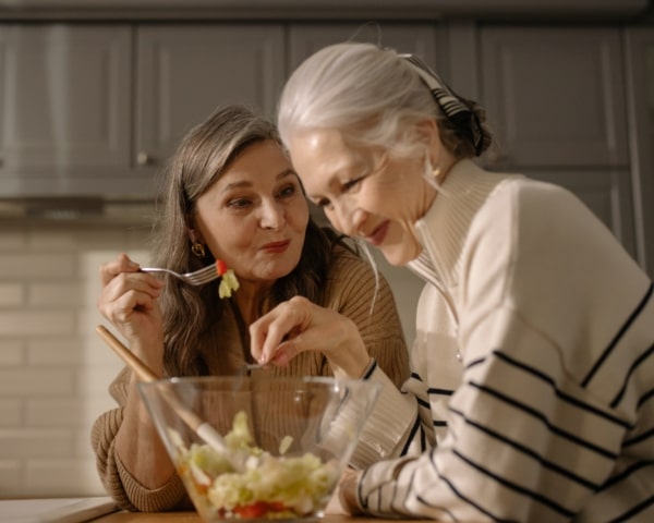 Dos mujeres mayores disfrutando y compartiendo una ensalada juntas.