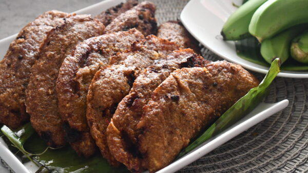 Macabeos de carne servidos en una hoja de plátano con plátanos verdes al fondo.