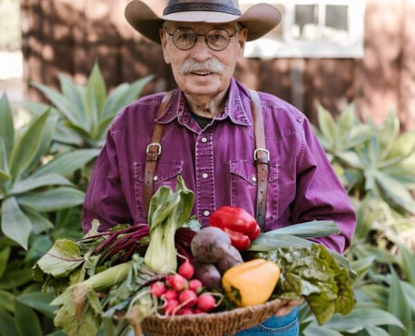 Hombre mayor con sombrero sosteniendo una cesta de verduras frescas.