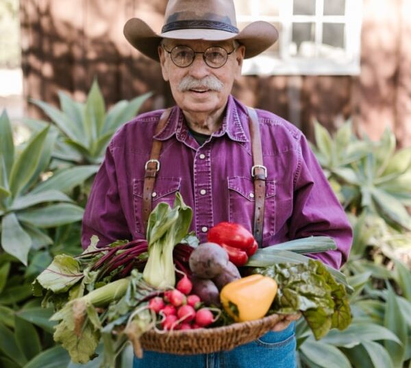 Hombre mayor con sombrero sosteniendo una cesta de verduras frescas.