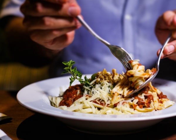 Persona con un plato de pasta con salsa roja y queso.