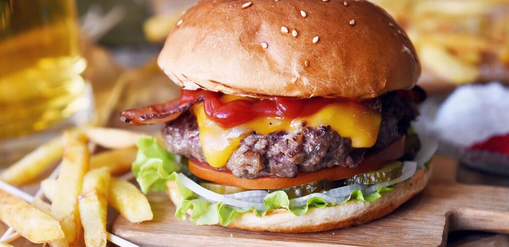 Hamburguesa con queso y tocino servida con papas fritas y cerveza.