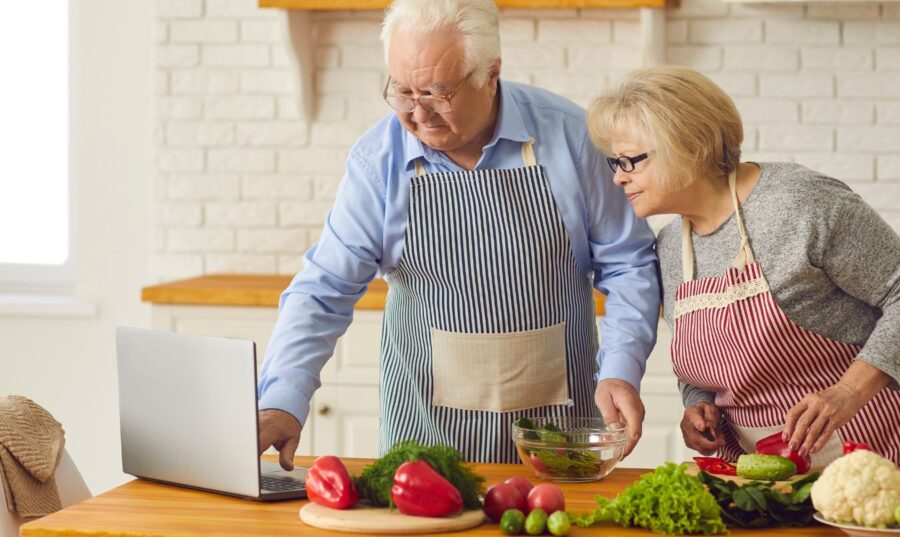 Pareja de adultos mayores buscando recetas en línea mientras cocinan juntos.