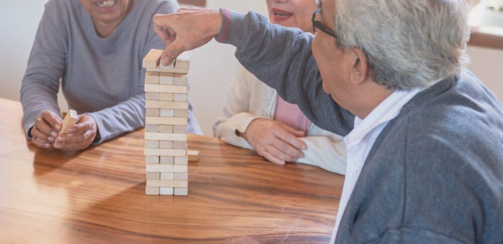 Tres personas mayores disfrutando de un juego de destreza con bloques de madera.