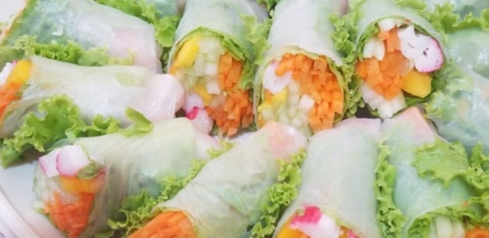 Rollitos de Primavera recién preparados, colocados en un plato blanco, rellenos de coloridas vegetales como zanahorias, lechuga y rábanos, envueltos en papel de arroz translúcido.