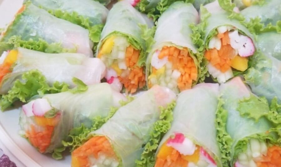 Rollitos de Primavera recién preparados, colocados en un plato blanco, rellenos de coloridas vegetales como zanahorias, lechuga y rábanos, envueltos en papel de arroz translúcido.