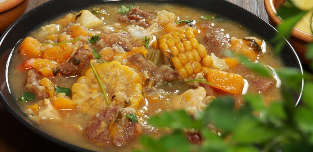 Plato de sancocho con carne, vegetales y viandas acompañado de arroz blanco y aguacate.