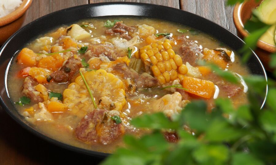 Plato de sancocho con carne, vegetales y viandas acompañado de arroz blanco y aguacate.