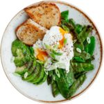 Un plato saludable con tostadas de pan integral, aguacate en rodajas, guisantes salteados y un huevo escalfado, decorado con cebollín y semillas de chía.