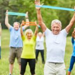 Grupo de adultos mayores realizando ejercicio al aire libre usando bandas de resistencia, mejorando su fuerza y flexibilidad.