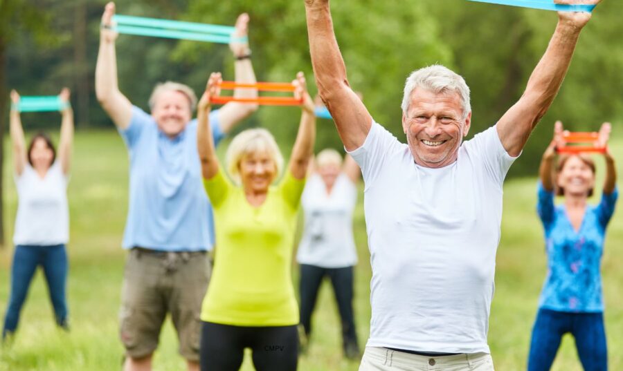 Grupo de adultos mayores realizando ejercicio al aire libre usando bandas de resistencia, mejorando su fuerza y flexibilidad.