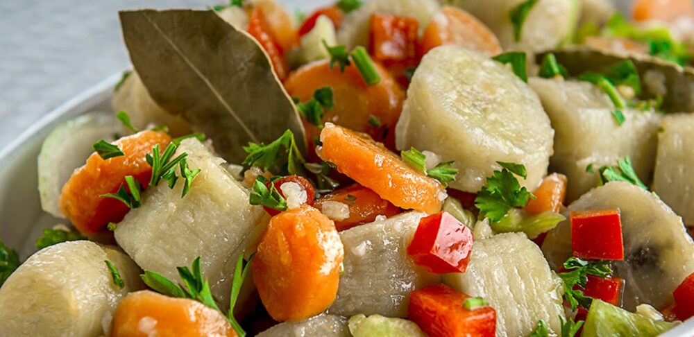 Primer plano de un plato de guineítos en escabeche con rodajas de zanahoria, pimientos rojos y verdes, adornado con hojas de laurel y perejil fresco.