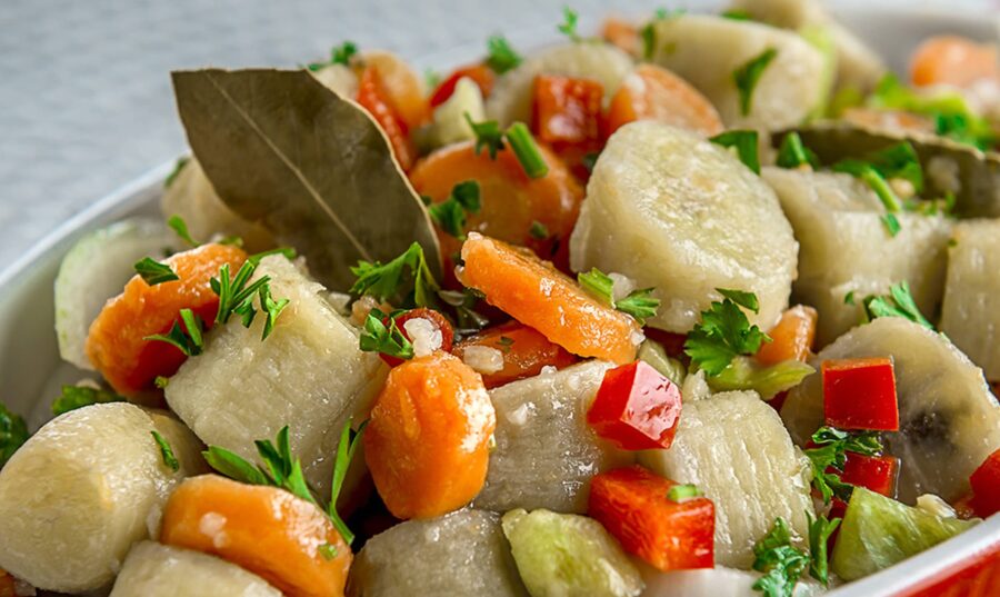 Primer plano de un plato de guineítos en escabeche con rodajas de zanahoria, pimientos rojos y verdes, adornado con hojas de laurel y perejil fresco.