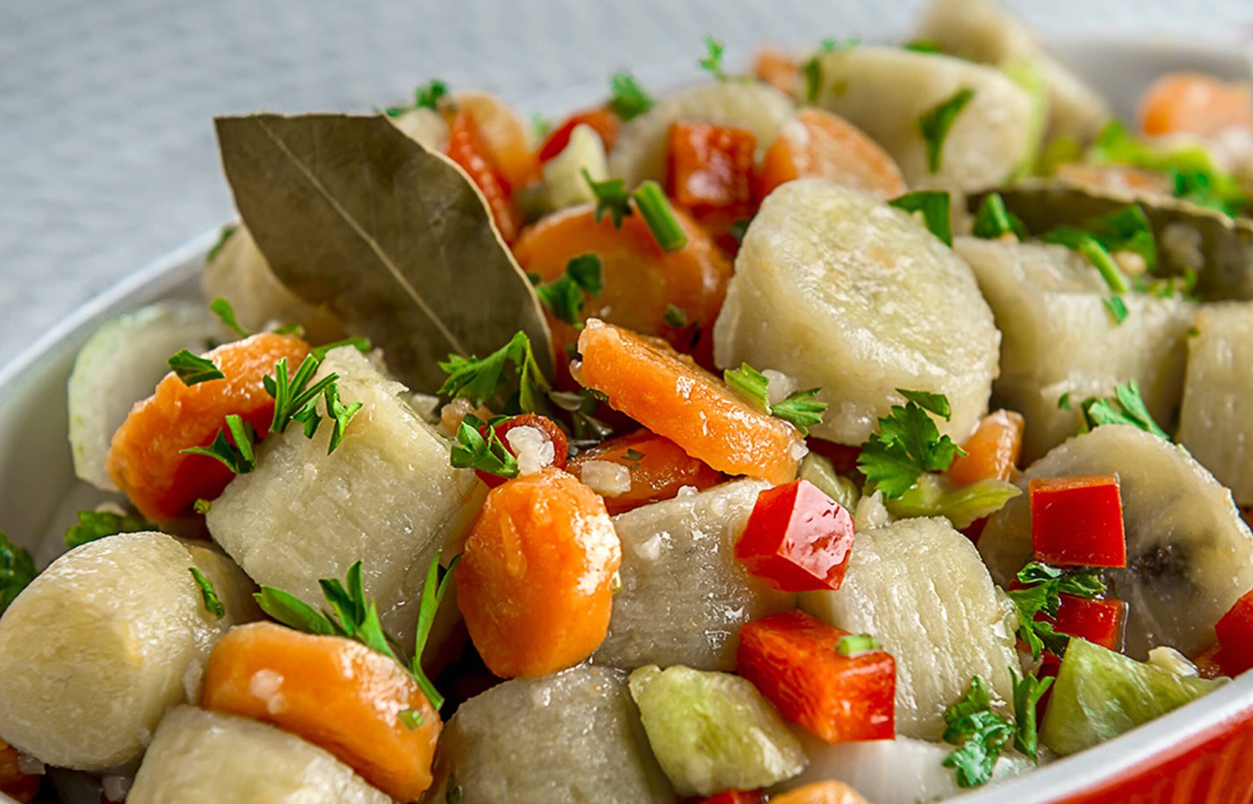 Primer plano de un plato de guineítos en escabeche con rodajas de zanahoria, pimientos rojos y verdes, adornado con hojas de laurel y perejil fresco.