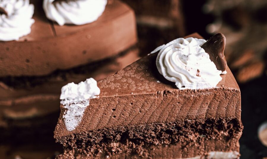 Un apetitoso pastel de chocolate con capas cremosas y decorado con crema batida, colocado en un plato oscuro junto a un tenedor y almendras, capturando un antojo irresistible de algo dulce.