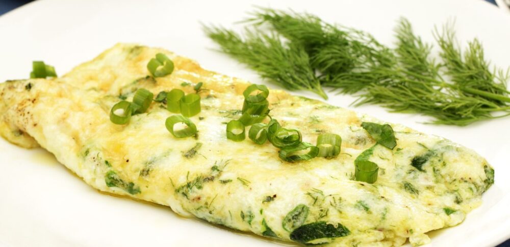 Tortilla de claras de huevo con hierbas frescas y cebollín sobre un plato blanco, acompañada de eneldo.