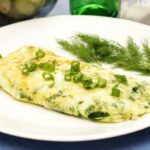 Tortilla de claras de huevo con hierbas frescas y cebollín sobre un plato blanco, acompañada de eneldo.