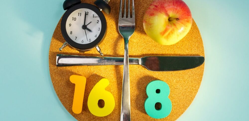 Plato con reloj, cubiertos y manzana que representa el método 16:8 de ayuno intermitente.