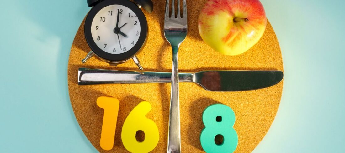 Plato con reloj, cubiertos y manzana que representa el método 16:8 de ayuno intermitente.