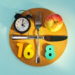 Plato con reloj, cubiertos y manzana que representa el método 16:8 de ayuno intermitente.