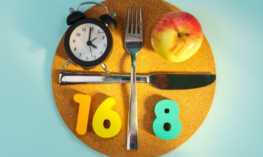 Plato con reloj, cubiertos y manzana que representa el método 16:8 de ayuno intermitente.