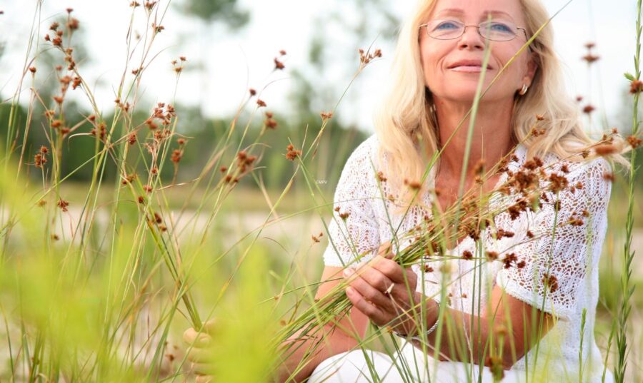 Mujer mayor rodeada de plantas medicinales en un campo natural, simbolizando los beneficios de los adaptógenos para la salud mental, inmunológica y emocional.