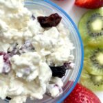 Tazón de requesón bajo en grasa con pasas, acompañado de fresas y rodajas de kiwi, ideal para una merienda saludable en adultos mayores.