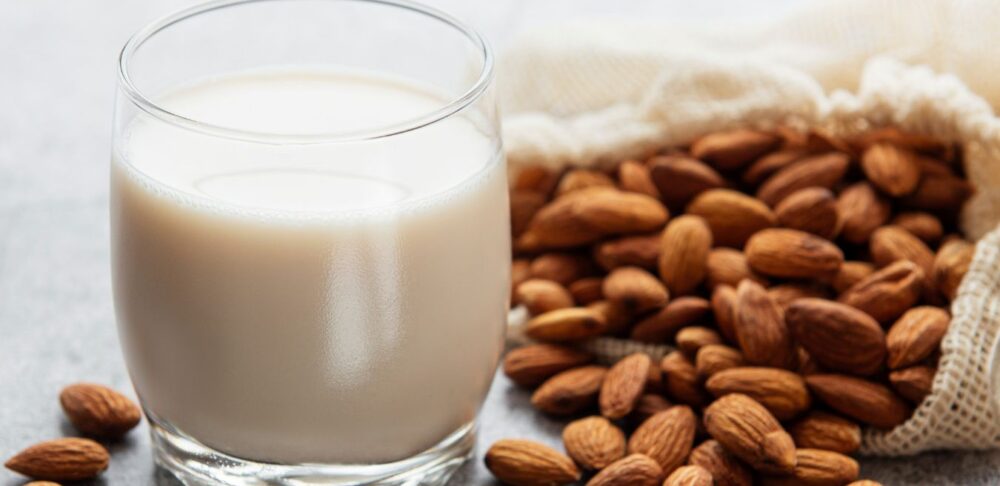 Leche de almendra en vaso junto a almendras enteras, ejemplo de bebida vegetal como alternativa no láctea a la leche.