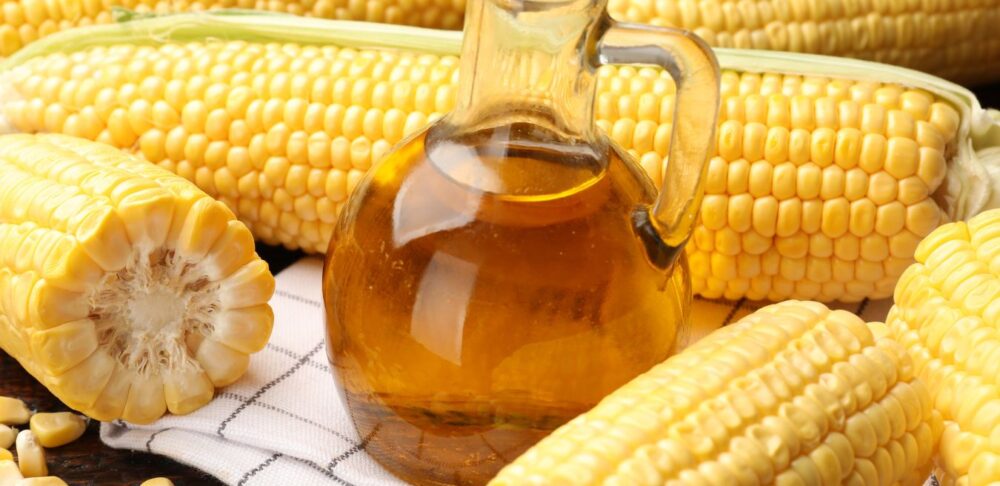 Jarabe de maíz alto en fructosa en frasco, rodeado de mazorcas de maíz, que simboliza el origen del HFCS utilizado en alimentos procesados.