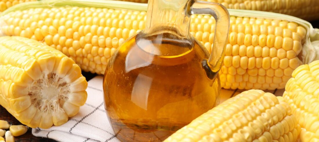 Jarabe de maíz alto en fructosa en frasco, rodeado de mazorcas de maíz, que simboliza el origen del HFCS utilizado en alimentos procesados.