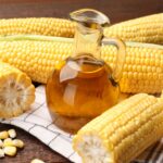 Jarabe de maíz alto en fructosa en frasco, rodeado de mazorcas de maíz, que simboliza el origen del HFCS utilizado en alimentos procesados.