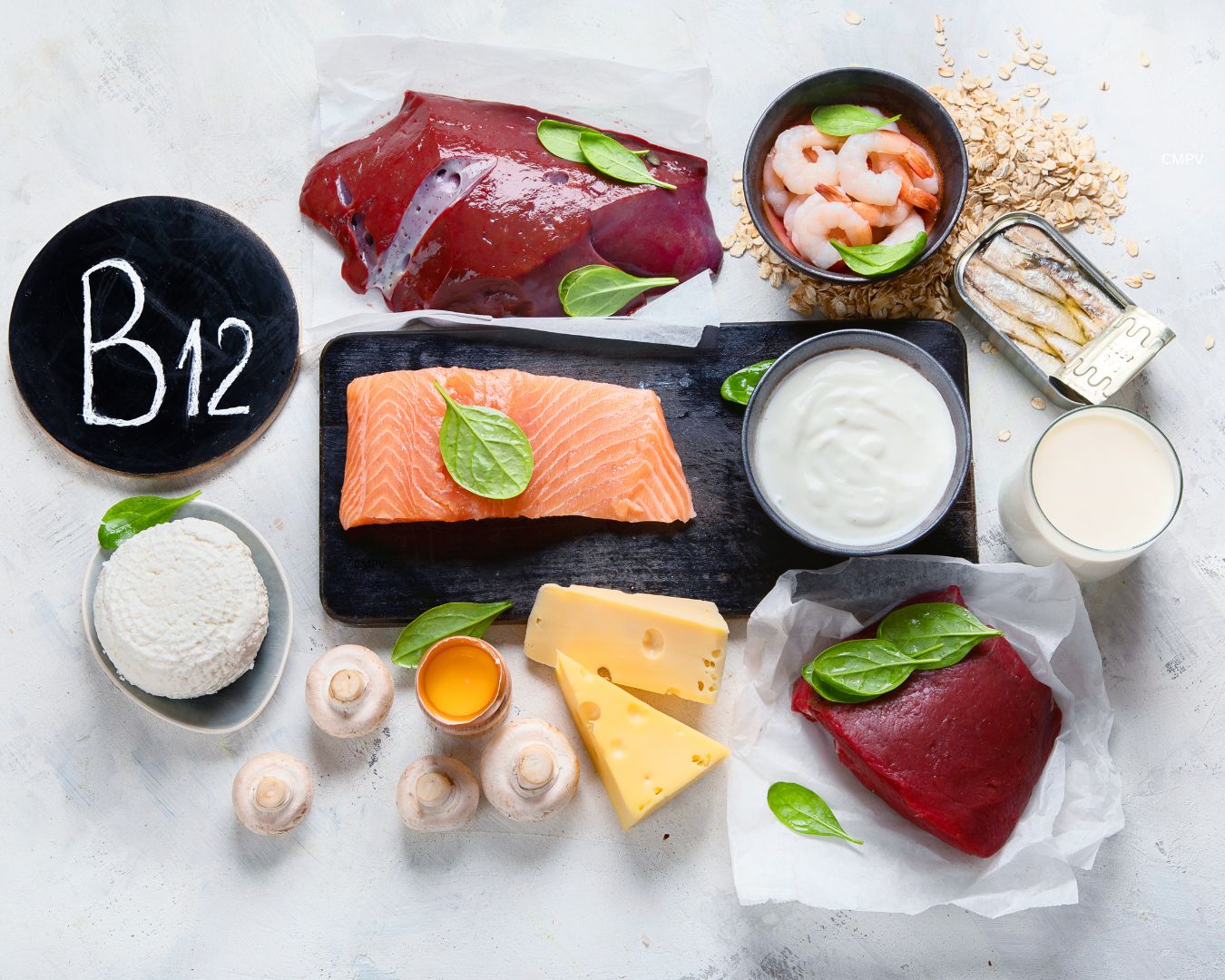 Fuentes alimenticias de vitamina B12 sobre una mesa, incluyendo salmón, hígado, carne de res, camarones, sardinas, leche, yogur, queso, huevo y cereales fortificados.