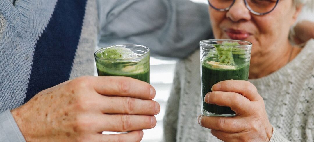 Pareja de adultos mayores sosteniendo bebidas verdes de matcha en un ambiente hogareño y relajado.