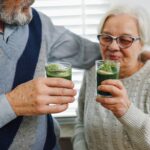 Pareja de adultos mayores sosteniendo bebidas verdes de matcha en un ambiente hogareño y relajado.