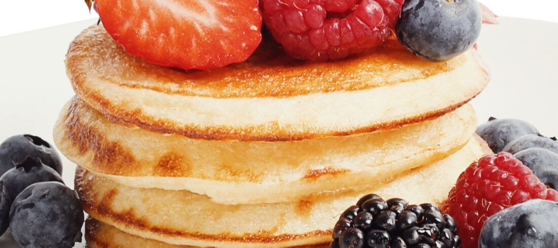 Plato con una torre de panqueques cubierta con fresas, frambuesas, moras y arándanos, un ejemplo de alimentos que aportan calorías y energía al organismo.