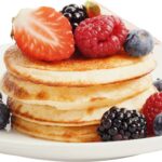Plato con una torre de panqueques cubierta con fresas, frambuesas, moras y arándanos, un ejemplo de alimentos que aportan calorías y energía al organismo.