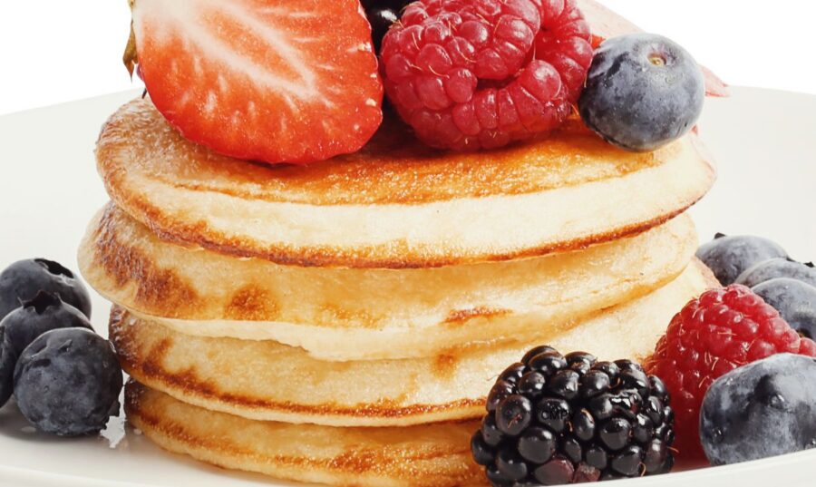 Calorías y Energía: Un Desayuno con Panqueques y Frutas Frescas Plato con una torre de panqueques cubierta con fresas, frambuesas, moras y arándanos, un ejemplo de alimentos que aportan calorías y energía al organismo.