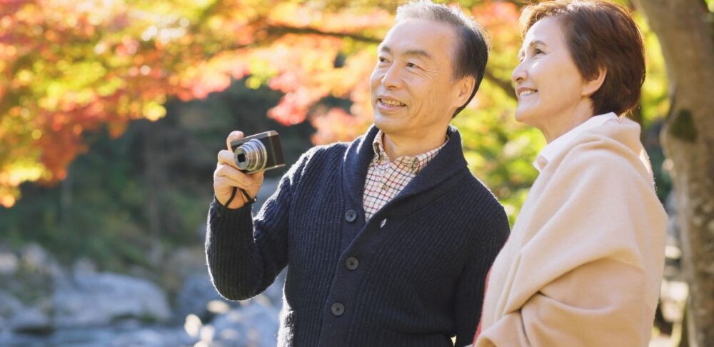 Pareja de adultos mayores disfrutando de un paseo al aire libre en un parque otoñal, un estilo de vida activo y saludable que puede ayudar a reducir el riesgo de cáncer.