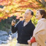 Pareja de adultos mayores disfrutando de un paseo al aire libre en un parque otoñal, un estilo de vida activo y saludable que puede ayudar a reducir el riesgo de cáncer.