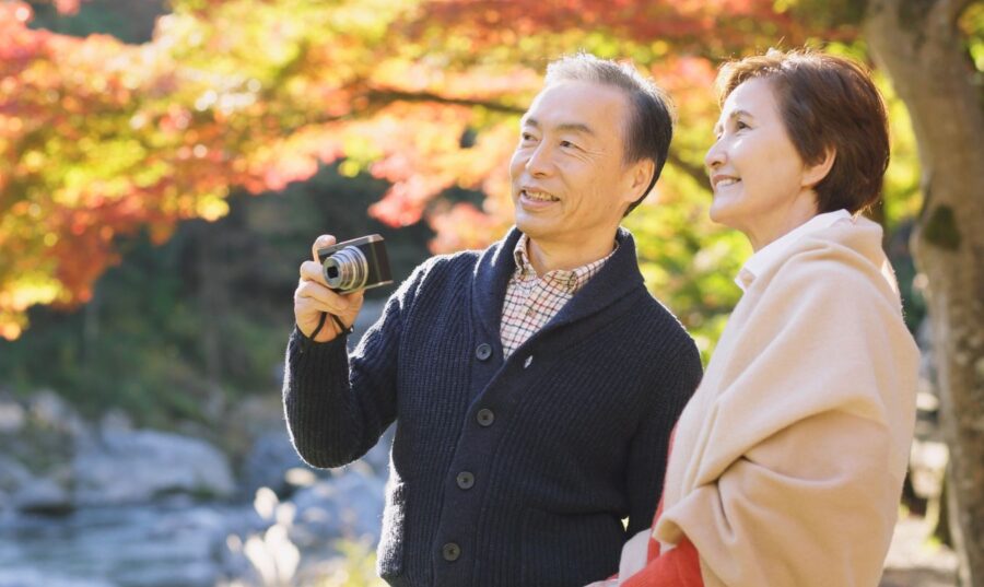 Pareja de adultos mayores disfrutando de un paseo al aire libre en un parque otoñal, un estilo de vida activo y saludable que puede ayudar a reducir el riesgo de cáncer.